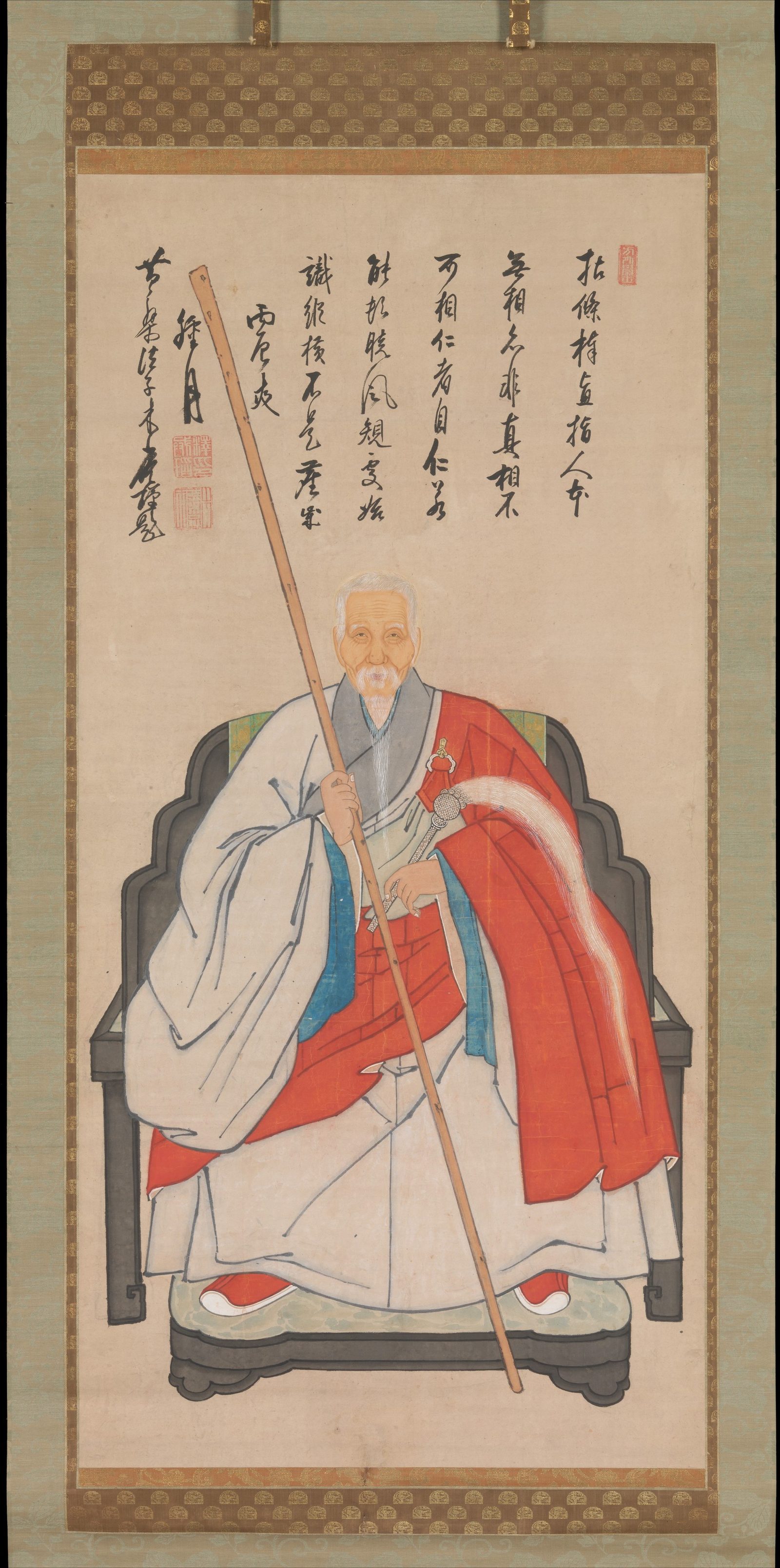 Hanging-scroll portrait of an elderly white-bearded monk in a lacquered chair, a red robe over pale garments, holding a long staff, with an inscription above