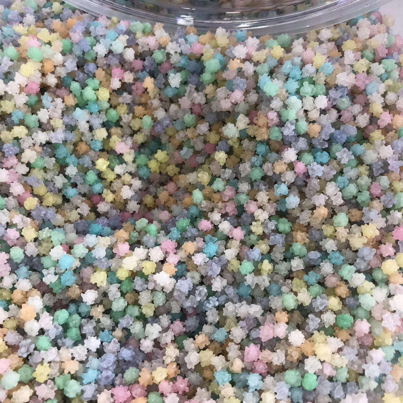 Close-up of hundreds of small pastel-colored star-shaped konpeitō candies filling a glass container