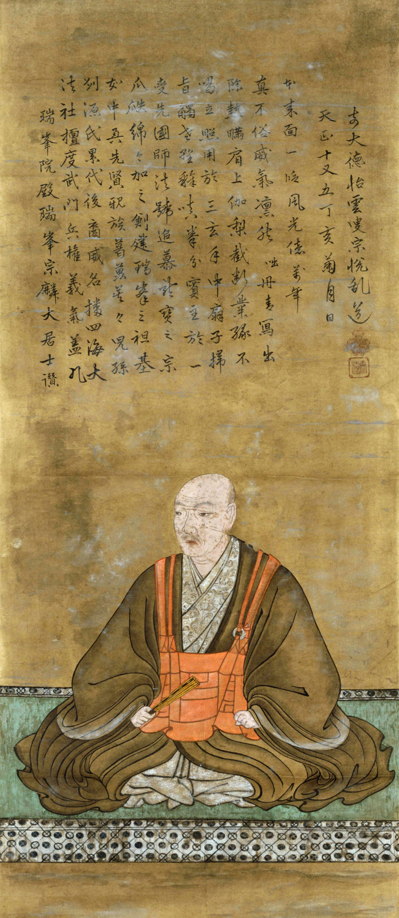 Ōtomo Sōrin as a shaven-headed lay monk in dark robes over an orange Buddhist surplice, fan in hand, on a green-edged mat under a long inscription dated 1587