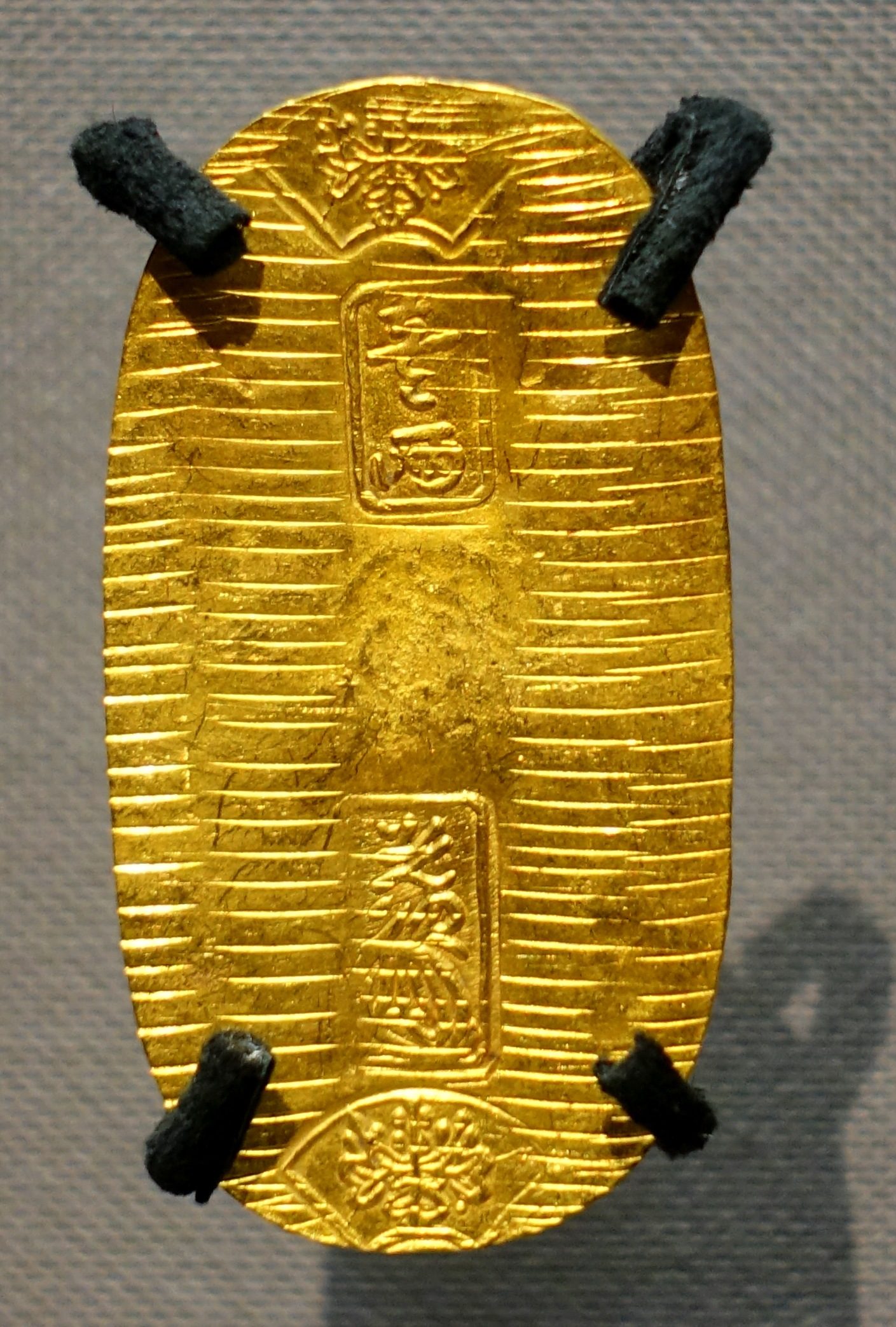 Gold Keichō koban: an oval coin hammered with fine horizontal lines, stamped 'one ryō', a mint master's seal and paulownia crests, clipped to a museum mount
