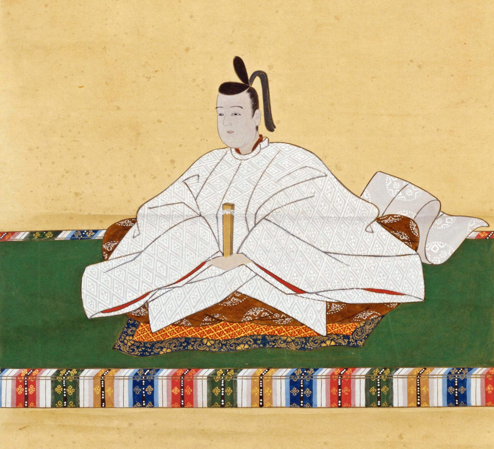文様入りのゆったりとした白い装束に小さな黒い冠をつけ、縞の縁のついた緑の畳に座って細い笏を持つ若い男性
